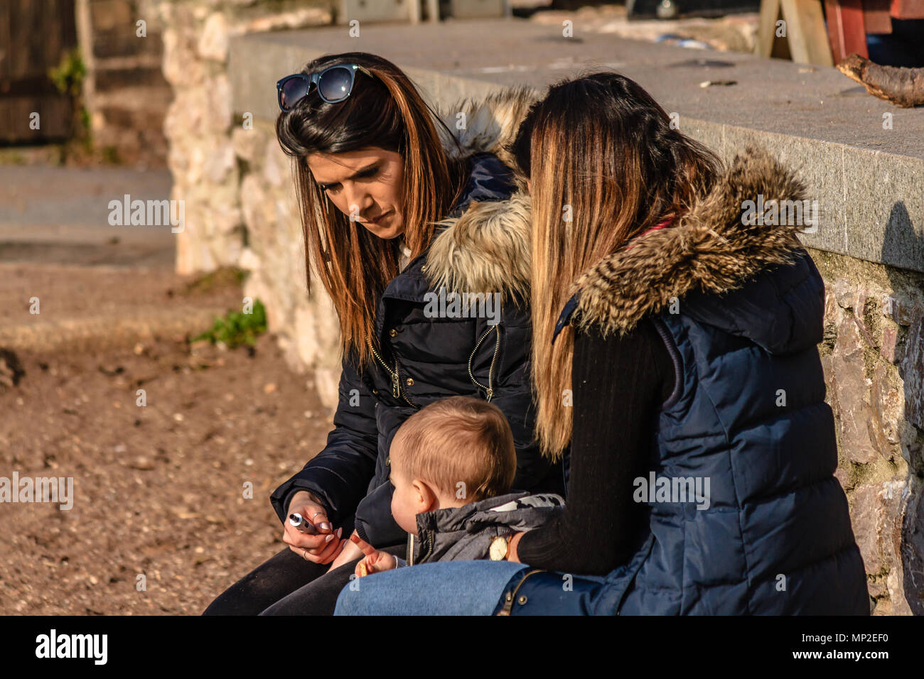 Deux femmes avec un bébé portant manteaux et assis sur la plage. Teignmouth, Devon. Feb 2018. Banque D'Images