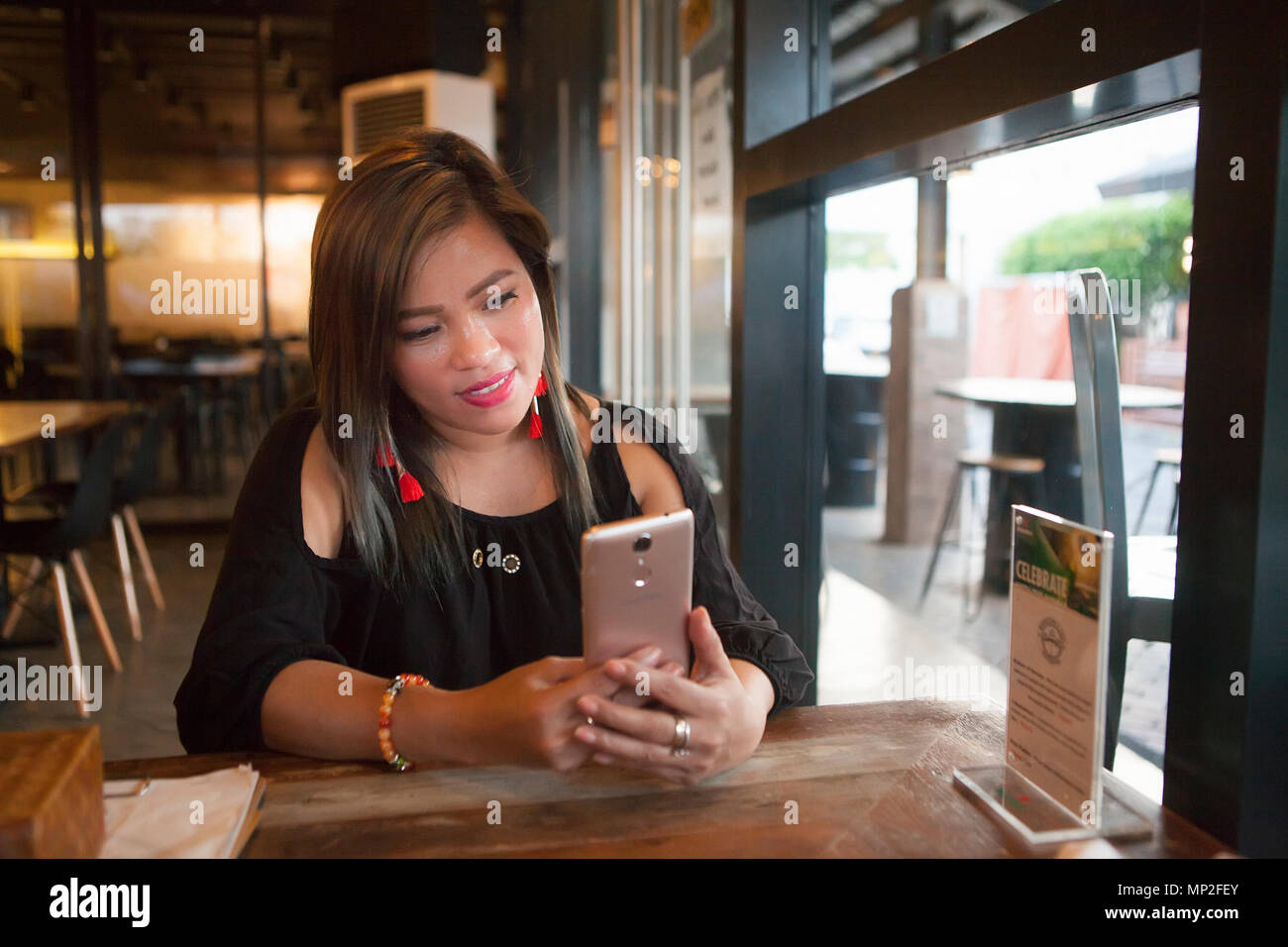 Heureux Young Asian woman des Philippines à la recherche de son smartphone à l'intérieur. Banque D'Images