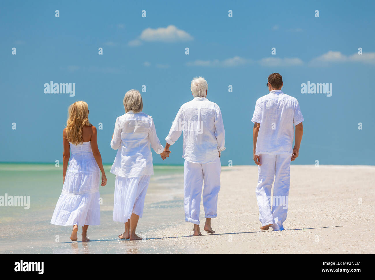 Vue arrière de quatre personnes, deux personnes âgées, des couples ou des générations, se tenir la main, marcher sur une plage tropicale vide Banque D'Images