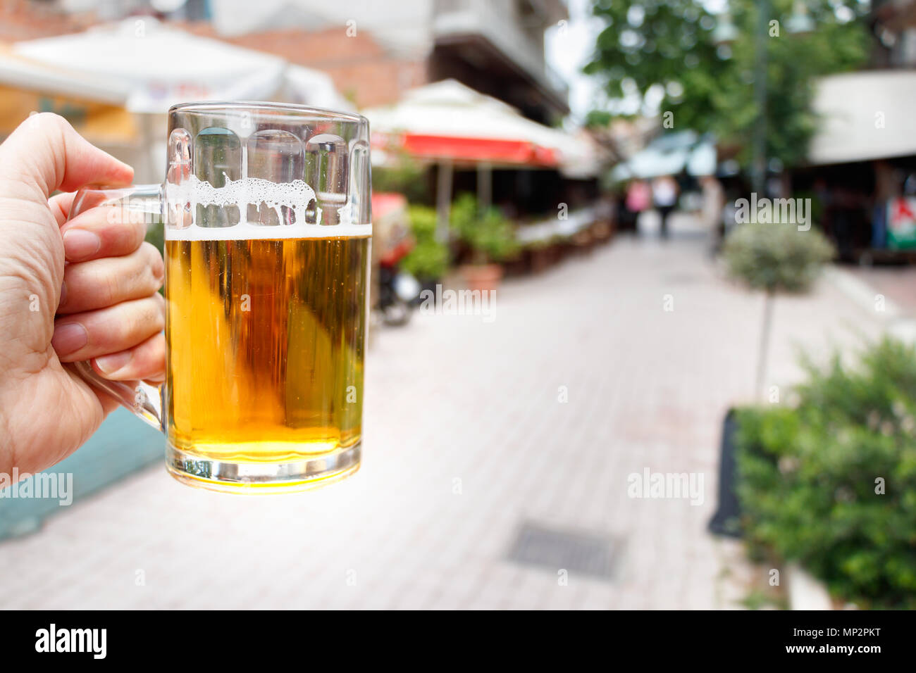 Un mâle main tenant un bocal en verre avec de la bière au cours d'un milieu urbain à l'extérieur, la lumière du soleil. Banque D'Images