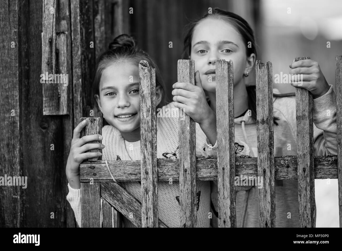 Portrait de deux soeurs filles adolescents regarder dehors derrière un village en bois clôture. Photo en noir et blanc. Banque D'Images