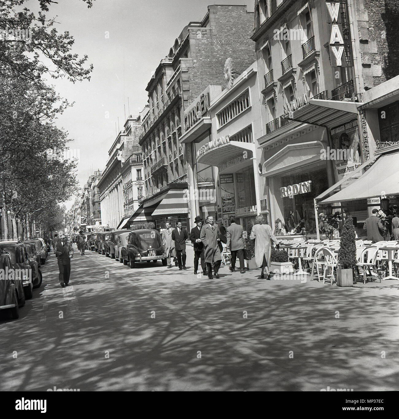 Années 1950, Paris et une vue sur le trottoir avec des voitures en stationnement bside magasins et cafés le long de l'Avenue des Champs-Elysees, montrant les marques françaises de Citreon, Rodin et le Broadway cinéma, Banque D'Images