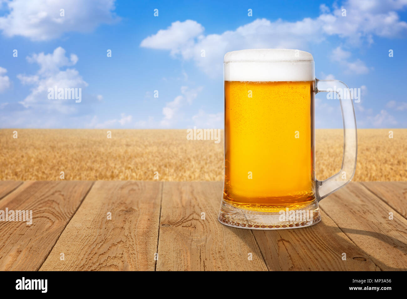 Chope de bière légère de mousse et de bulles sur table en bois contre champ de blé mûr sur journée d'été Banque D'Images