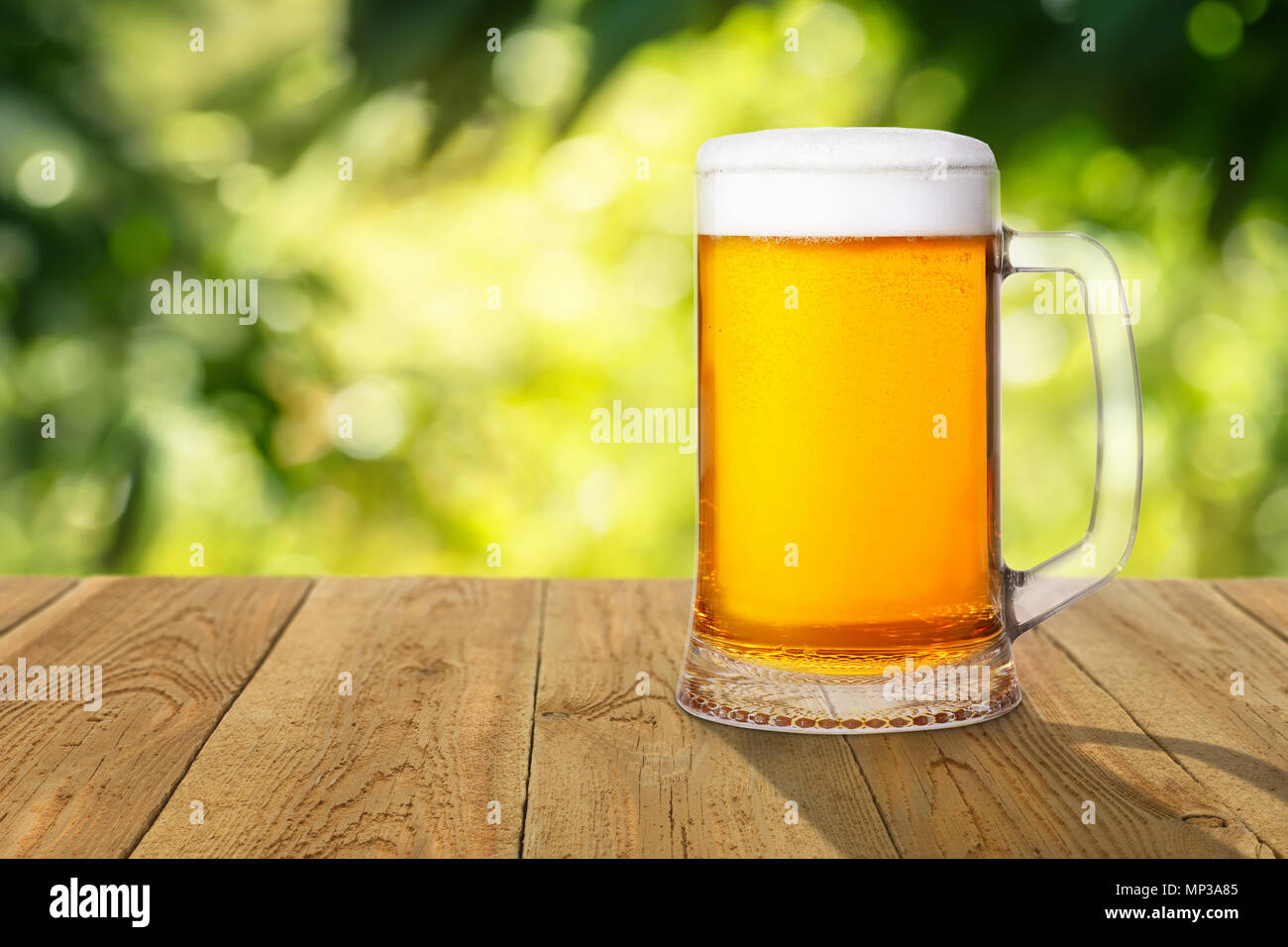 Chope de bière légère de mousse et de bulles sur table en bois avec fond flou vert Banque D'Images
