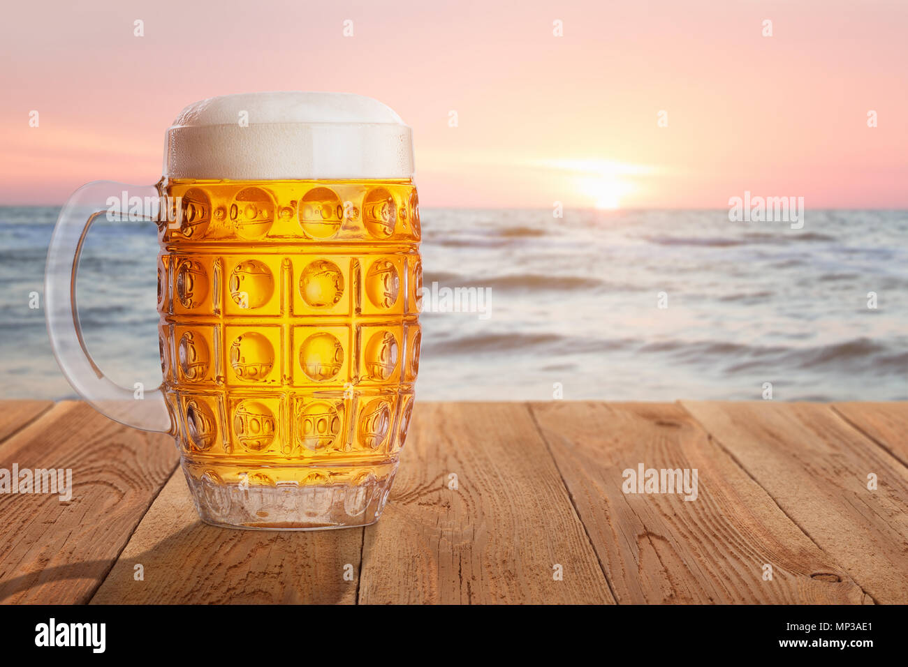 Chope de bière légère de mousse et de bulles sur table en bois contre la mer sur le coucher du soleil. Concept de repos et les vacances d'été Banque D'Images