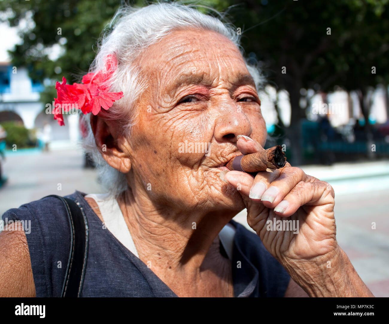 Vieille ridée femme fleur rouge de fumer un cigare. Santiago de Cuba, Cuba Banque D'Images