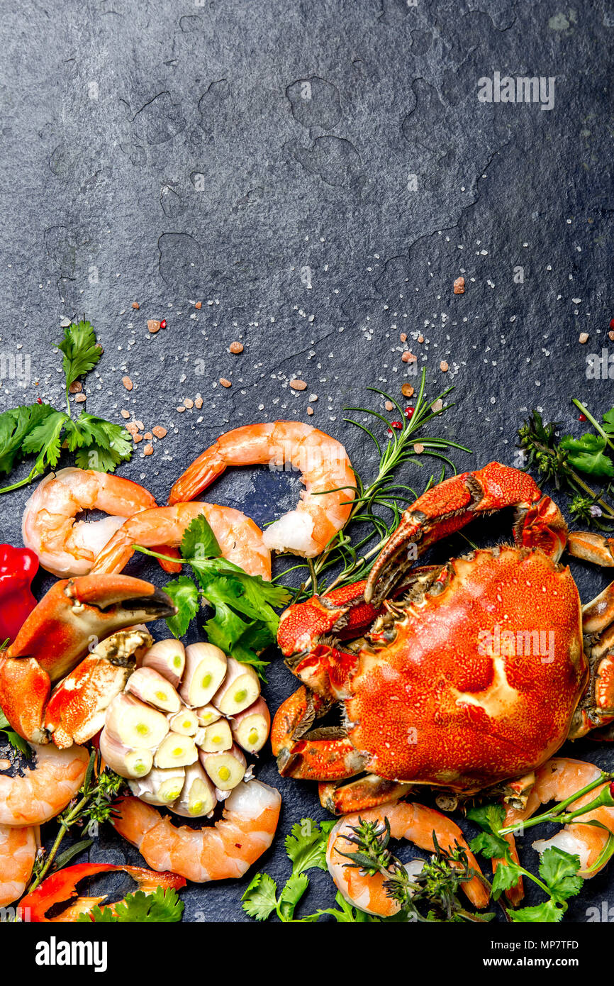 Produits frais et de fruits de mer crus - crevettes et crabes avec des herbes et épices sur fond gris foncé. Copier l'espace. Banque D'Images