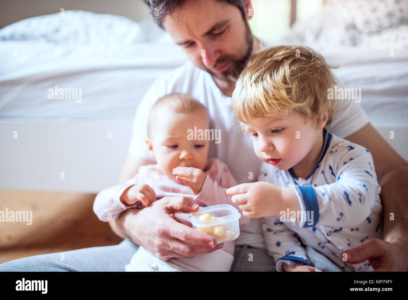Père tout-petits avec les enfants de manger de la nourriture de doigt dans la chambre à la maison. Banque D'Images