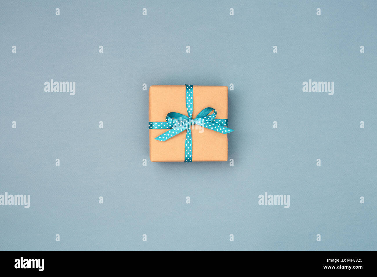 Une boîte-cadeau enveloppé dans du papier kraft et attaché avec du ruban bleu à pois blancs sur fond gris bleu. Vue de dessus, la place pour le texte. Maison de concept. Banque D'Images