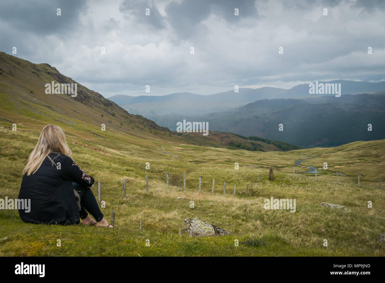 Une femme regarde à travers le paysage de la Cumbrie roulant haut de Honister Pass, alors que des nuages gris forme devant nous. Banque D'Images