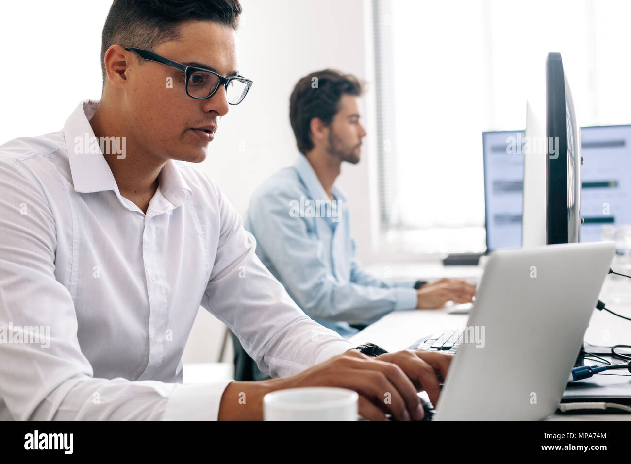Les développeurs de logiciels de bureau à travailler sur des ordinateurs. Homme portant des lunettes working on laptop computer in office. Banque D'Images