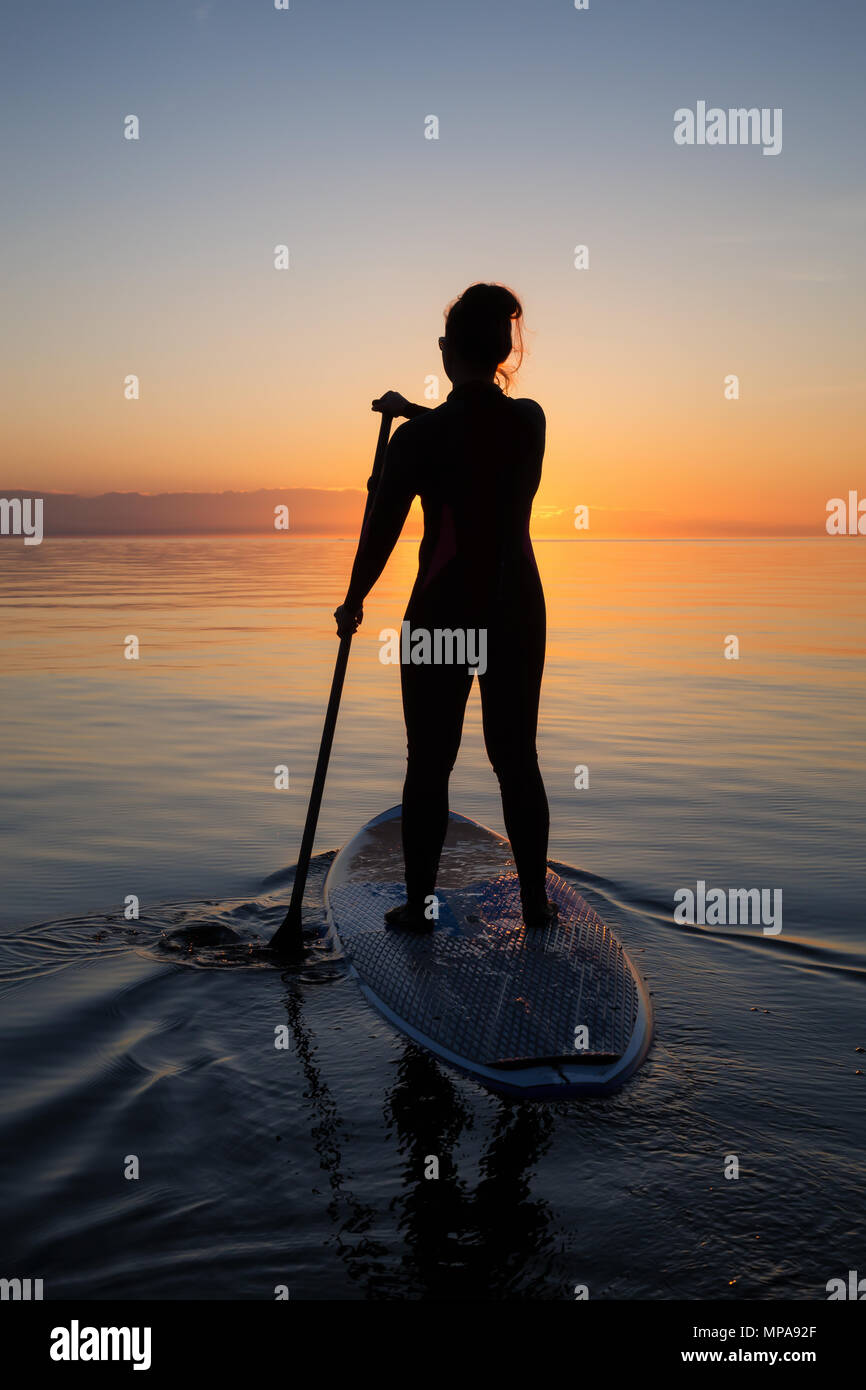 Fille d'aventure sur un paddle board est paddeling pendant un brillant et vibrant au coucher du soleil. Pris près de banques espagnoles, Vancouver, Colombie-Britannique, Canada. Banque D'Images