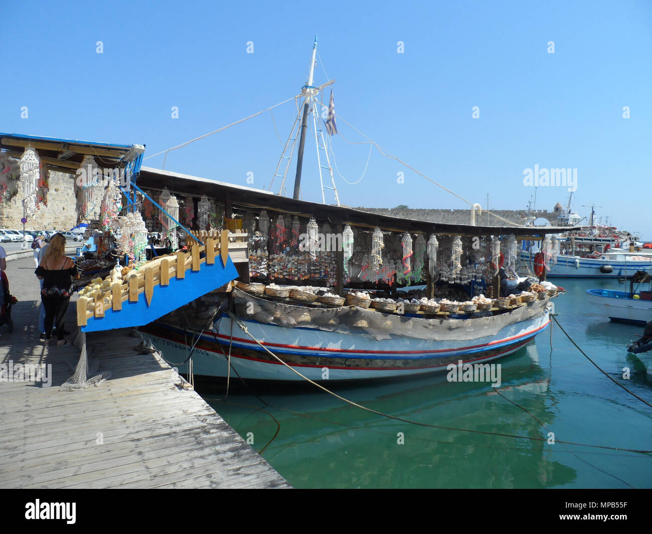 Les touristes parcourir les articles sur un bateau de pêche grec transformé en un magasin de souvenirs au port de Rhodes, Grèce. Banque D'Images