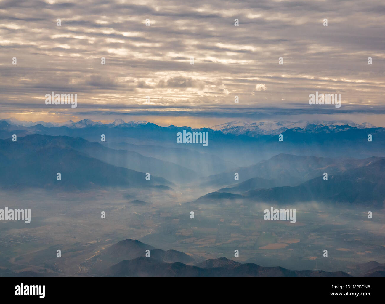 Vue depuis la fenêtre de l'avion volant au sud de Santiago, au Chili, avec des pics de montagne des Andes et les couches de nuages rompu par faisceaux de lumière tombant sur valley Banque D'Images