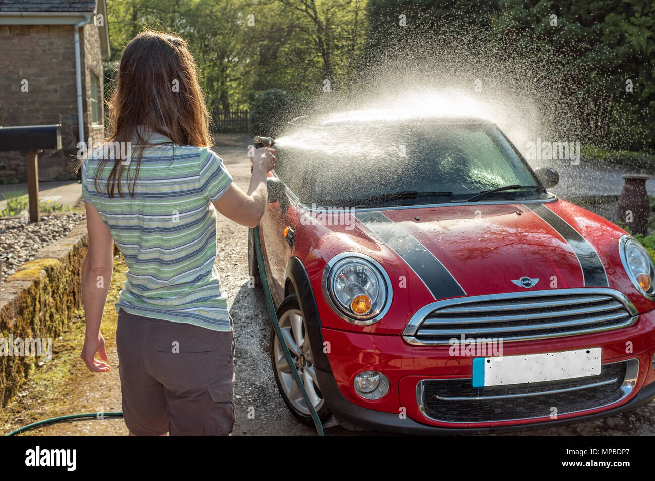 Une femme dans la quarantaine laver sa voiture dans le soleil. Banque D'Images