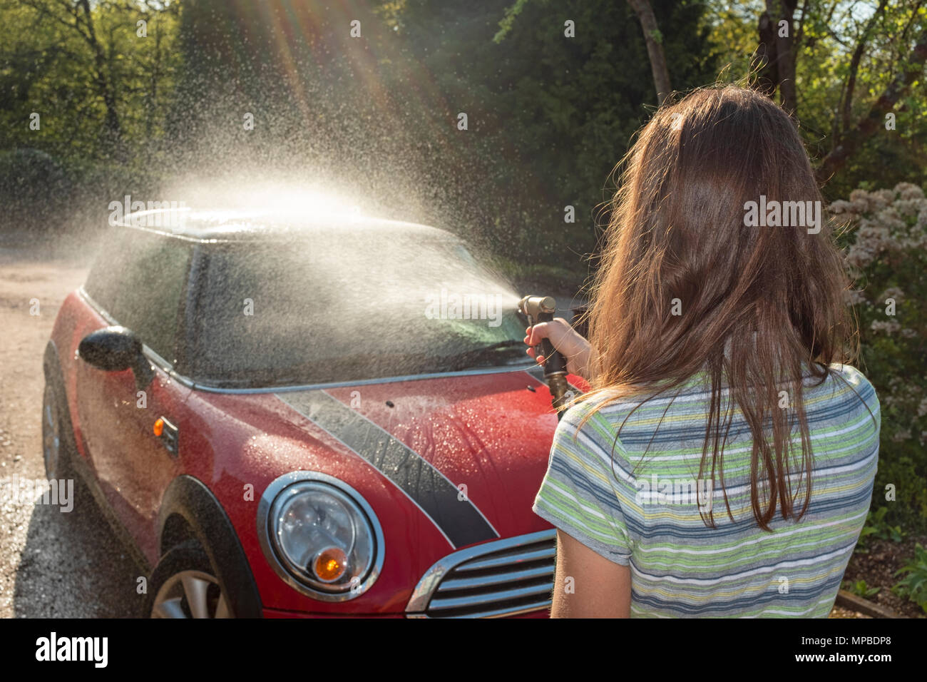 Une femme dans la quarantaine laver sa voiture dans le soleil. Banque D'Images