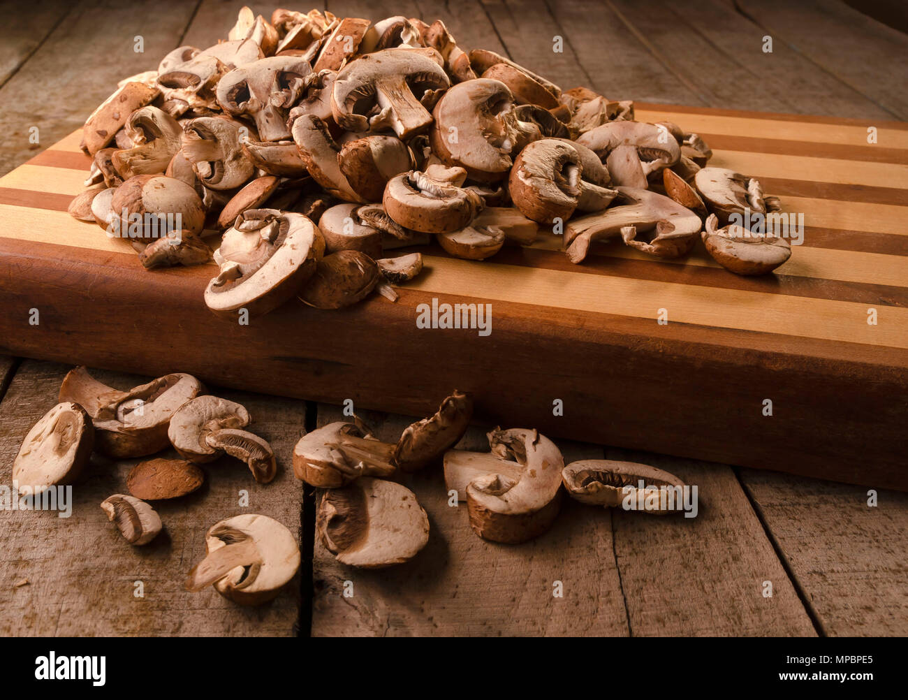 Les champignons crus en tranches fraîchement conserver sur une planche à découper en bois assis sur une surface en bois grange Banque D'Images