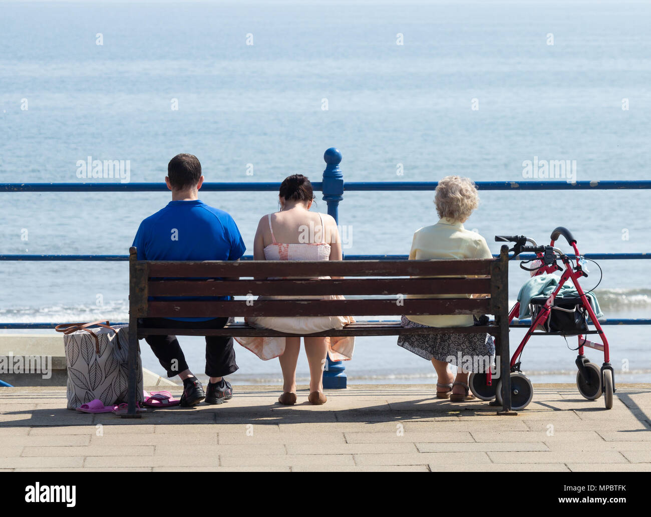 Femme âgée et jeune couple assis sur un banc avec vue sur la mer. UK Banque D'Images