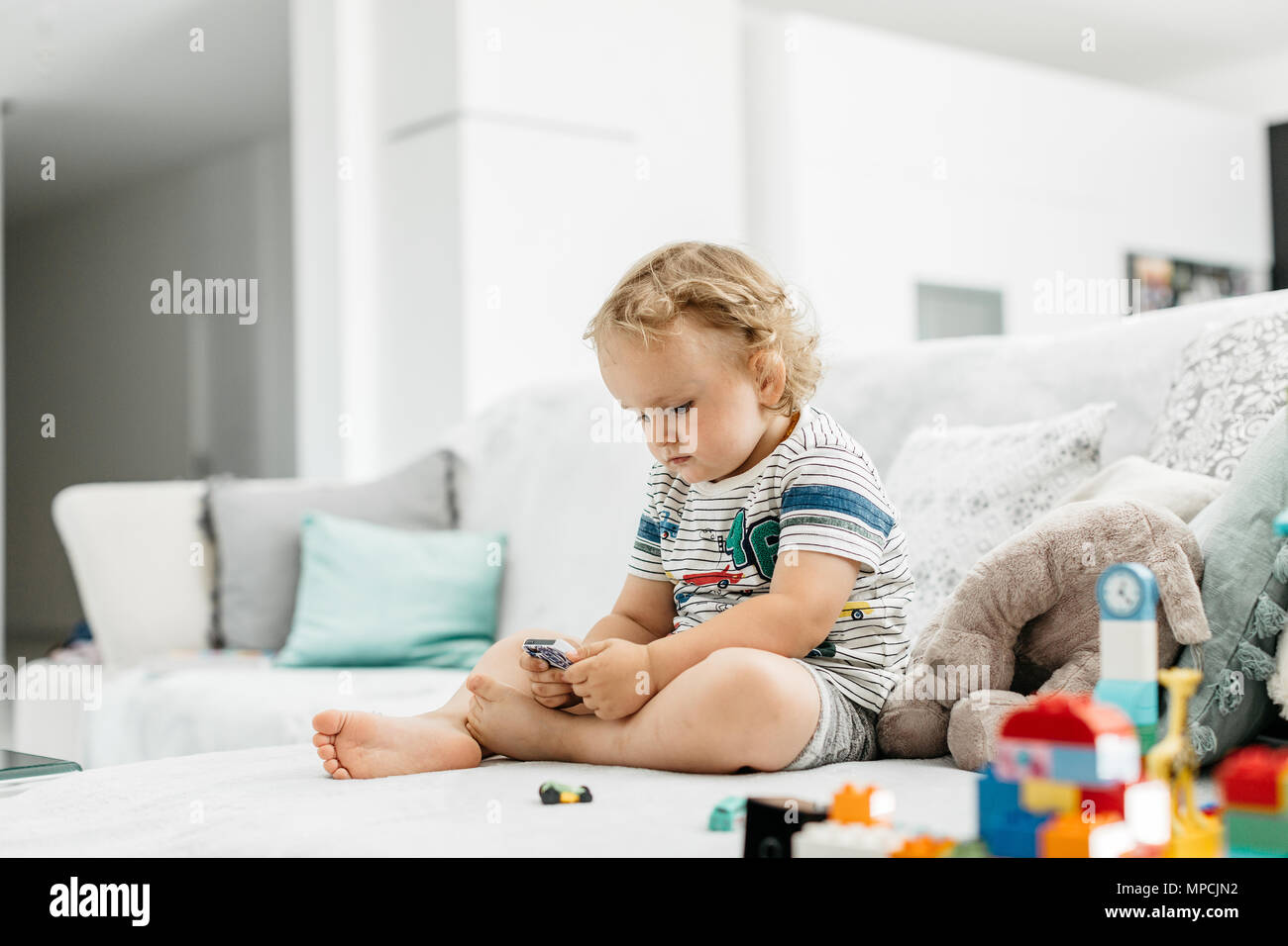 Un portrait d'un bébé garçon parcourt un cellulaire à la maison. Un petit enfant assis sur un canapé et jouer à des jeux sur téléphone mobile. Banque D'Images