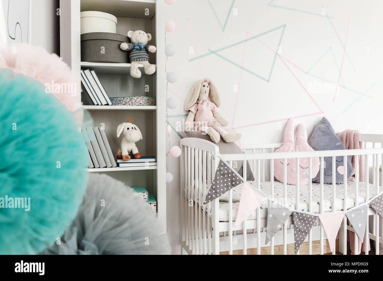Peluche lapin sur lit de bébé avec des bannières et des oreillers à côté de la tablette avec des jouets dans la chambre pastel Banque D'Images