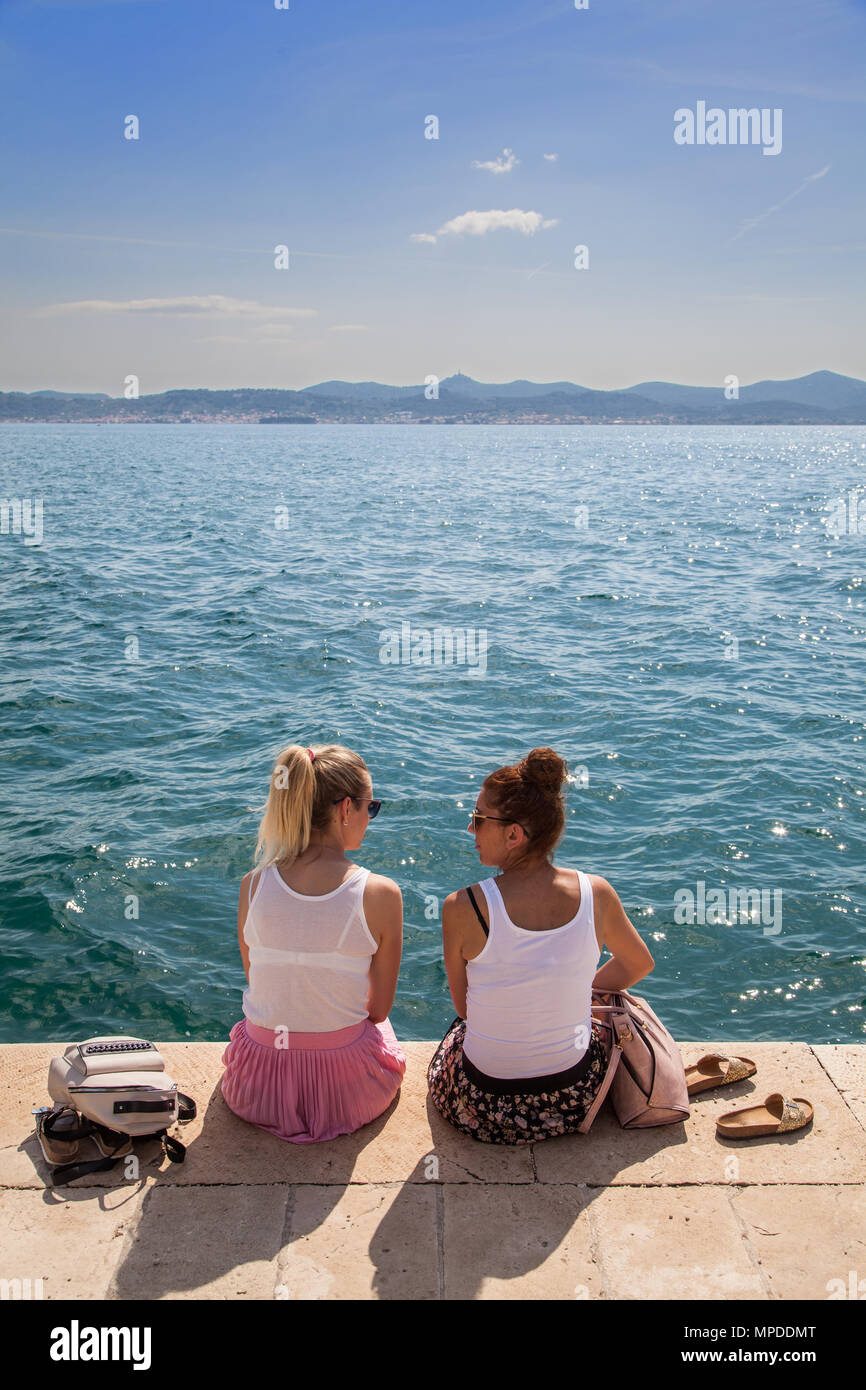 Deux jeunes femmes bénéficiant de parler assis au soleil sur la promenade du front de mer de la côte Adriatique port de Zadar Croatie Banque D'Images