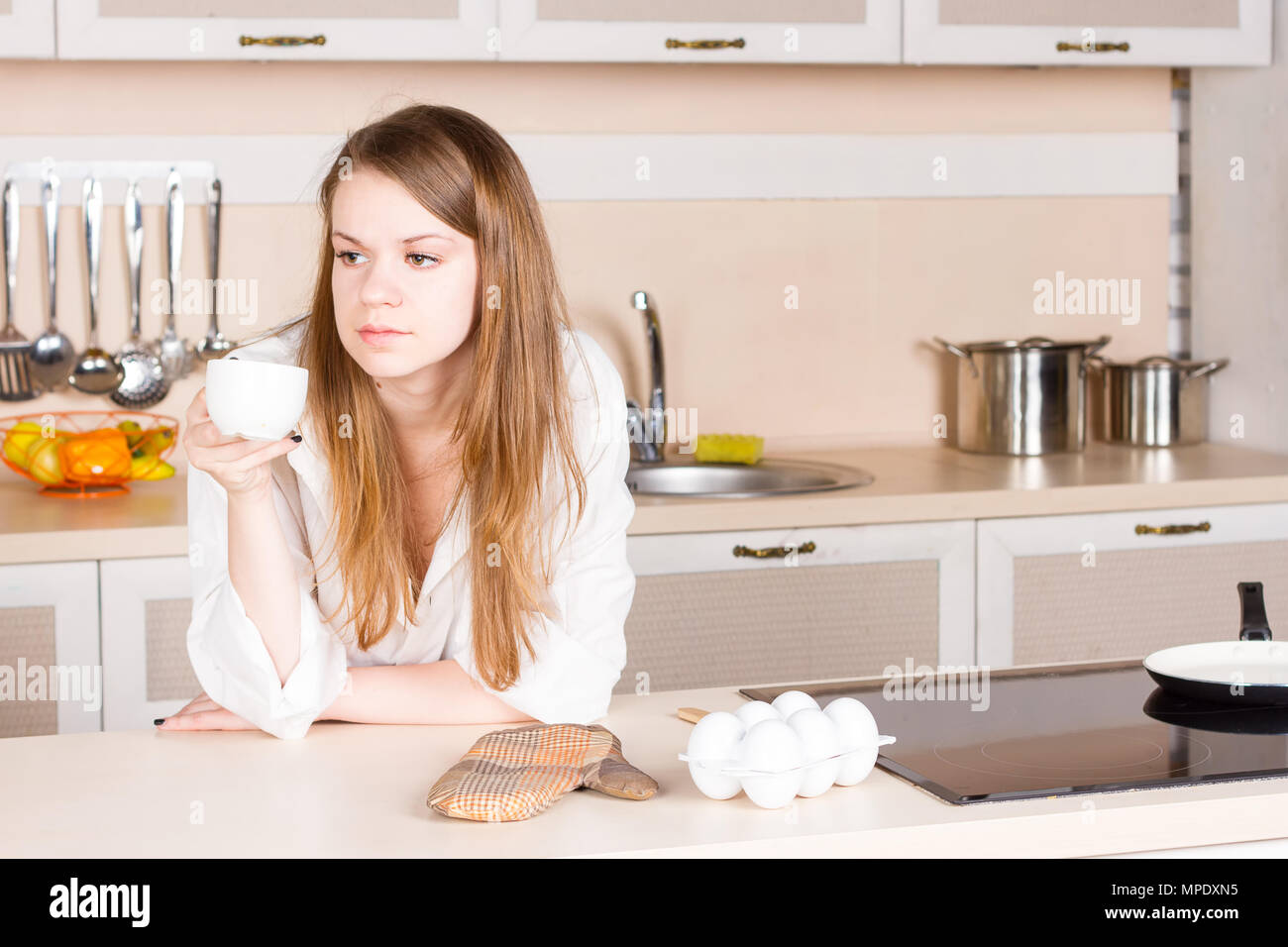 Girl in a white men's shirt avec longs cheveux est de boire du thé dans la cuisine le matin. Cadrage horizontal Banque D'Images