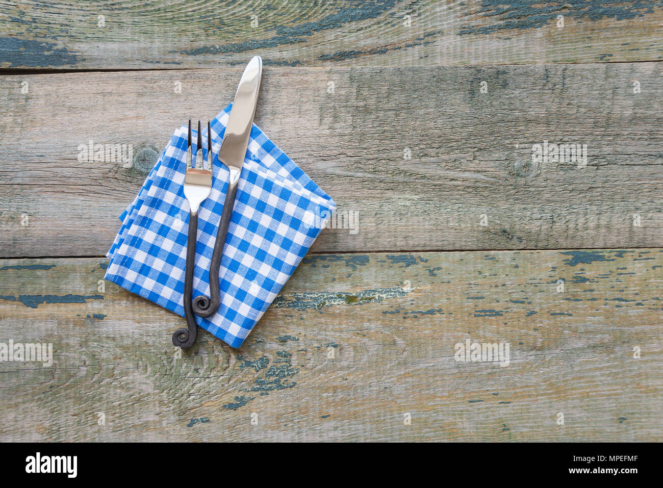 Fourchette et couteau artisanal forgé à damier et le bleu et blanc serviette reposent sur un fond de bois rugueux, avec l'espace pour le texte Banque D'Images