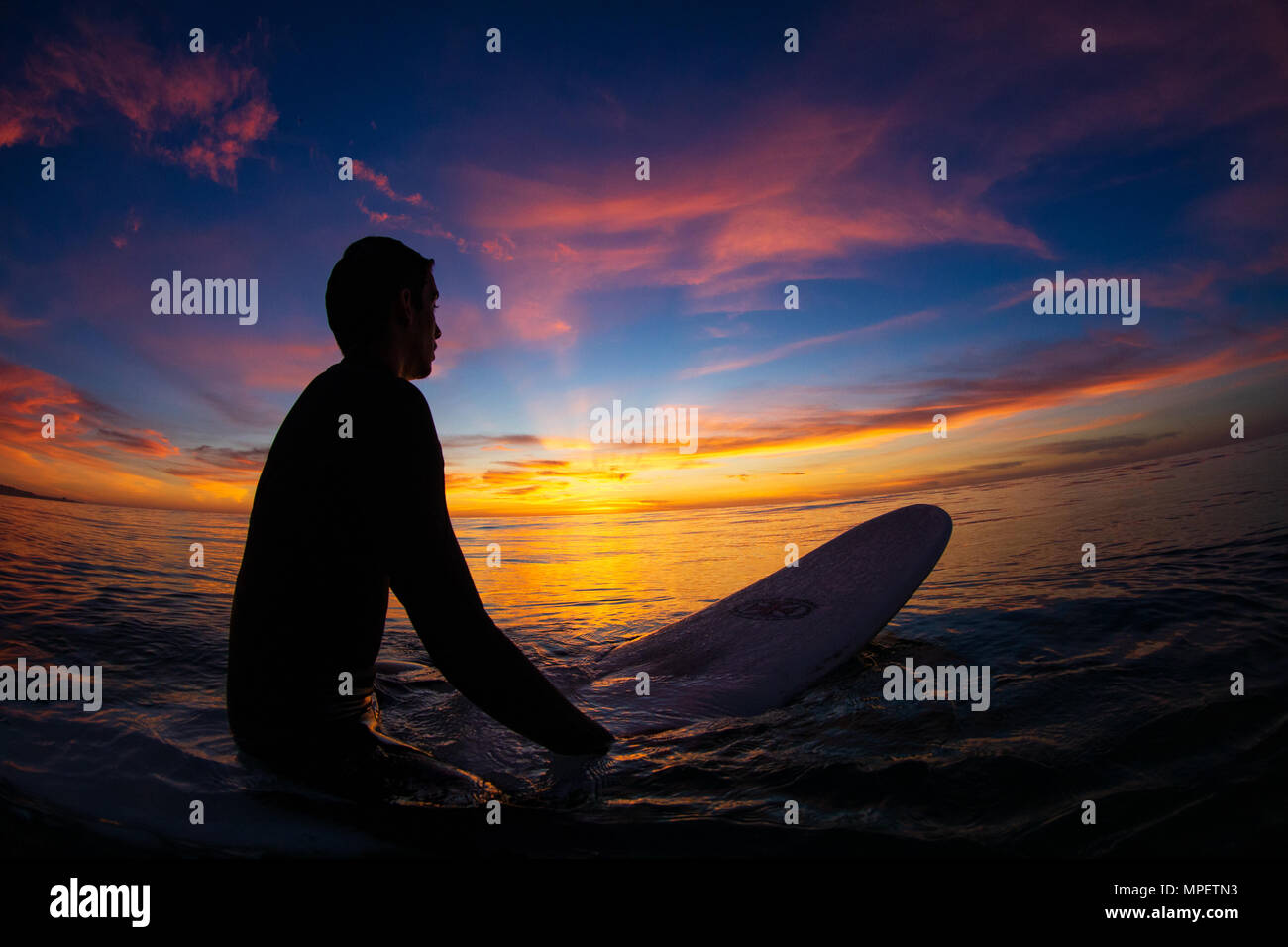 Surfer Latino Juan Gonzalez attend une vague sous un ciel de coucher du soleil à Torrey Pines State Beach, San Diego, CA. Banque D'Images