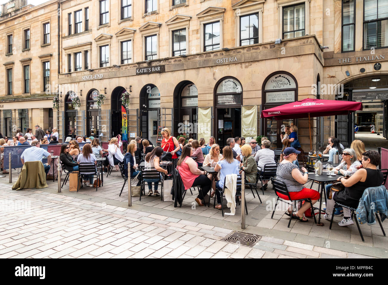 Les gens de boire et de parler à des tables en plein air dans la rue John, dans la région de la ville de marchands de Glasgow, Écosse, Royaume-Uni Banque D'Images