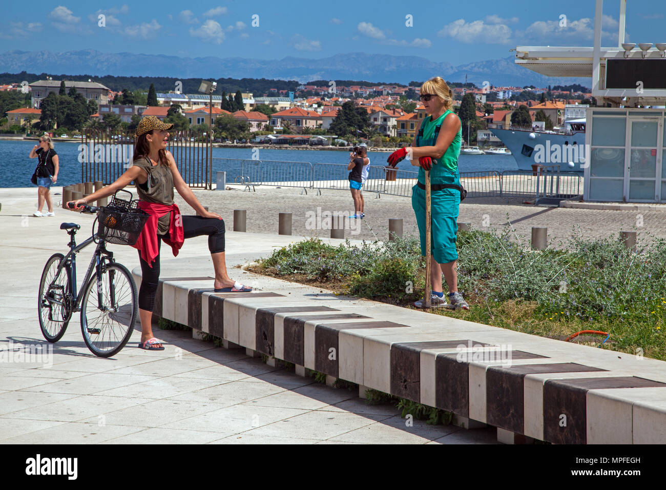 Chauffeur particulier femme appuyée sur une houe a cessé ses travaux de parler à un ami l'article de son cycle pushbike dans les jardins publics au port de Zadar Croatie Banque D'Images