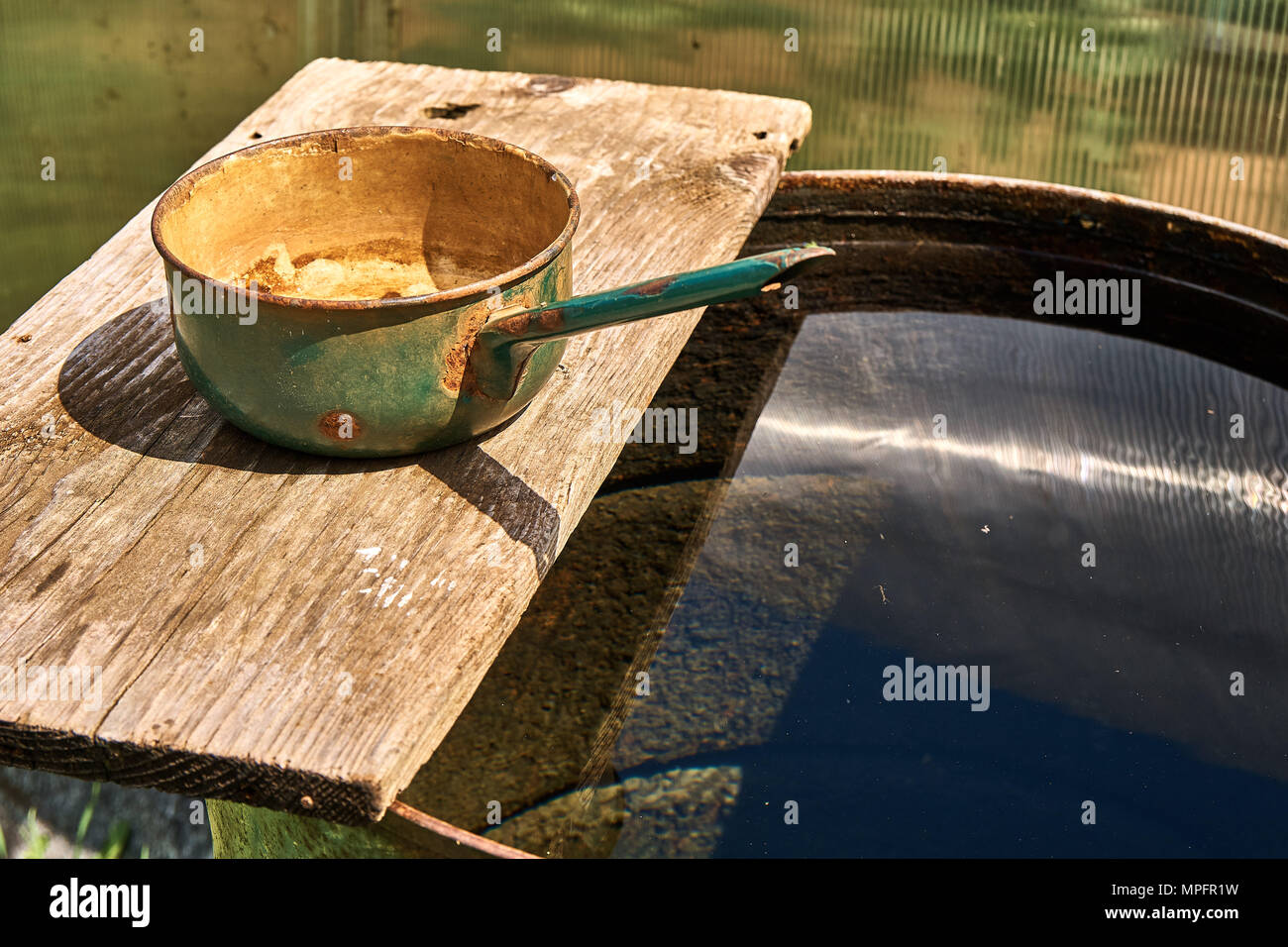 Baril de pluie rempli d'eau et louche de metall sur panneau de bois par beau temps Banque D'Images