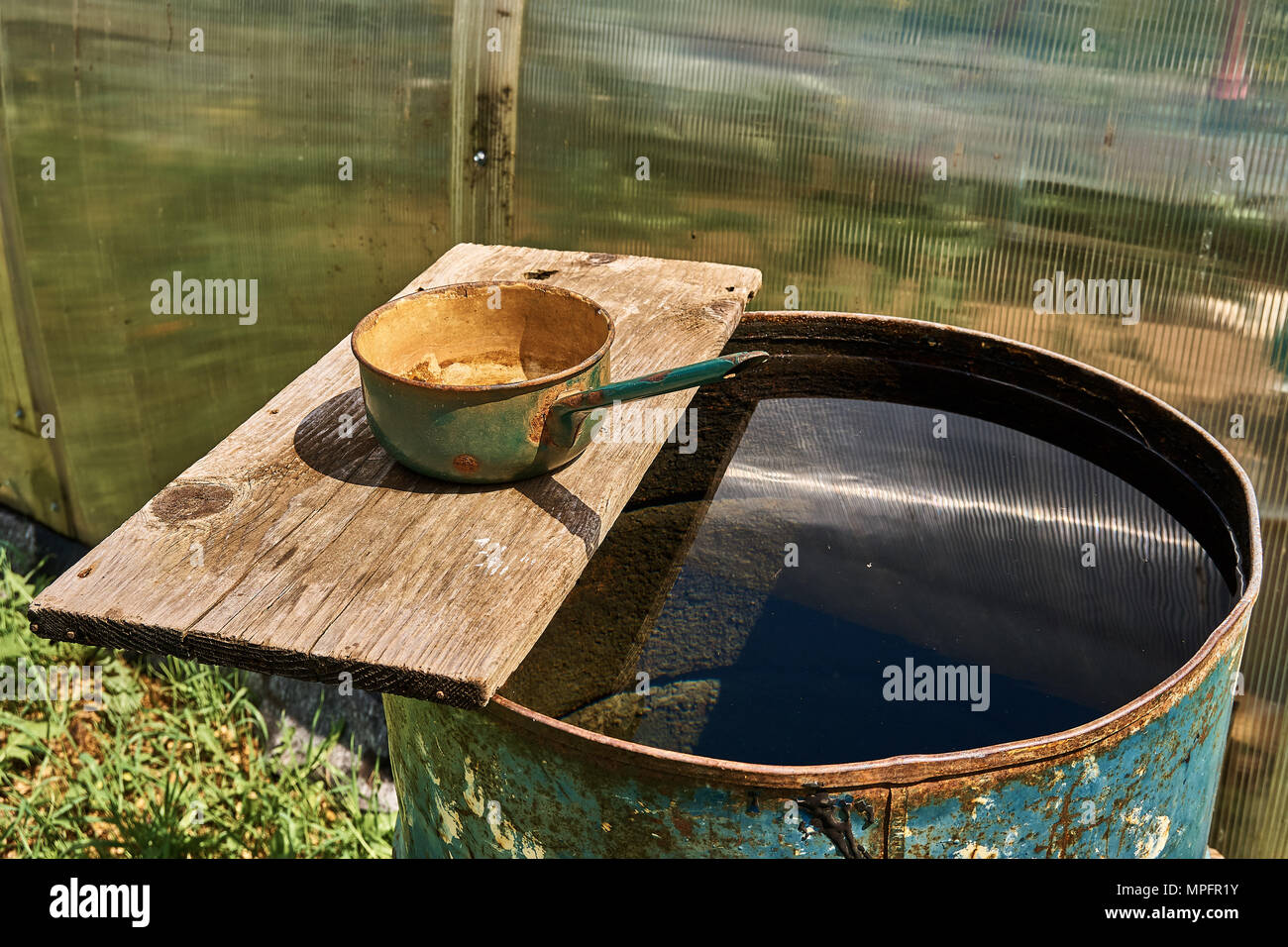 Baril de pluie rempli d'eau et louche de metall sur panneau de bois par beau temps Banque D'Images