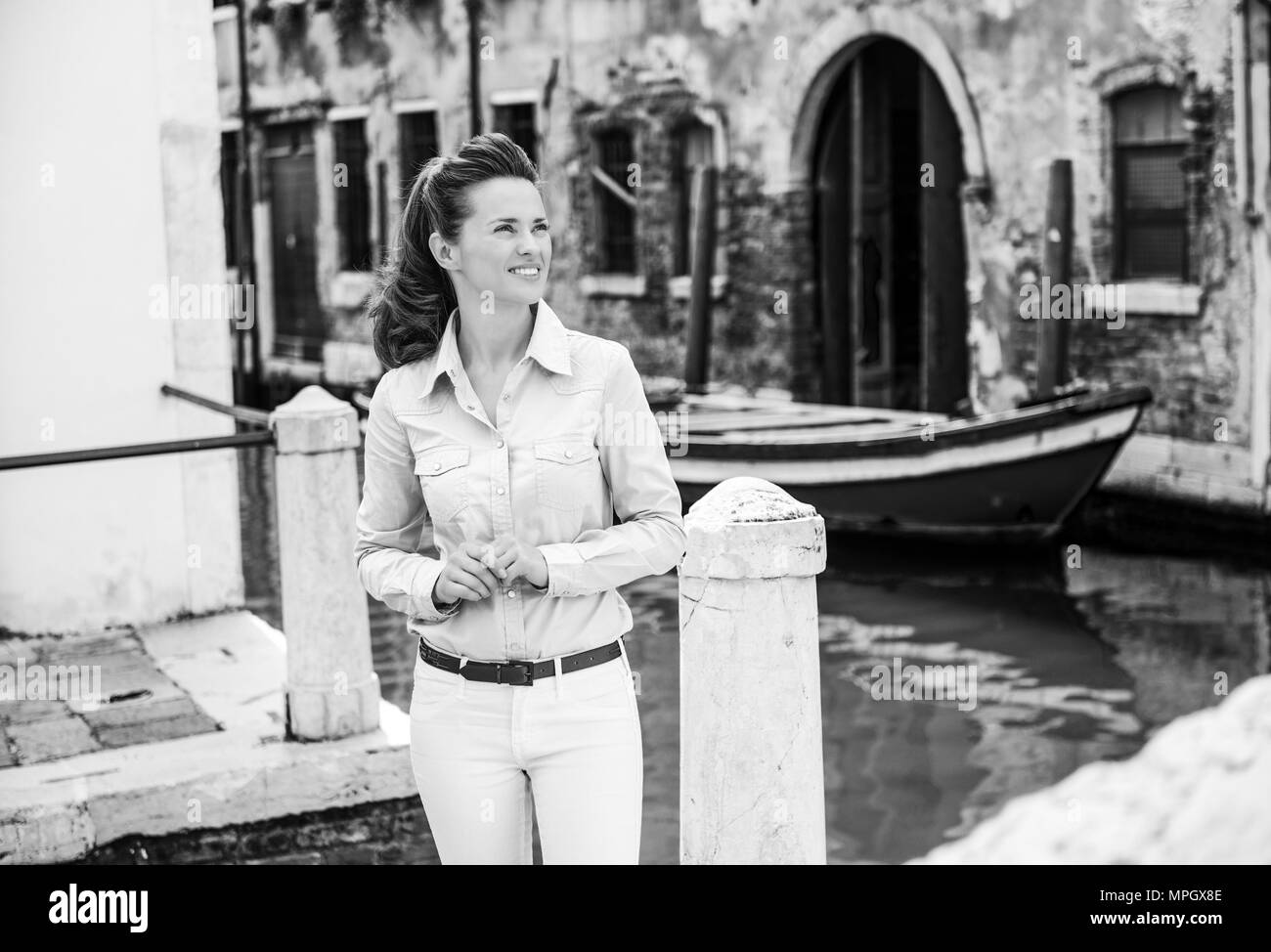 Looking up and smiling, une femme se tient debout près de l'un des nombreux canaux de Venise, jusqu'à dans la distance, se demandant où ses pieds se son nex Banque D'Images