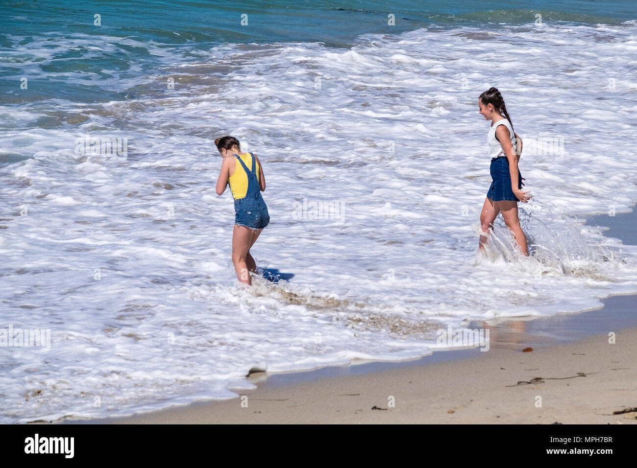 Jeunes filles adolescentes qui se sont promenées en vacances pagayant dans la mer à Sennen Cove, dans les Cornouailles. Banque D'Images