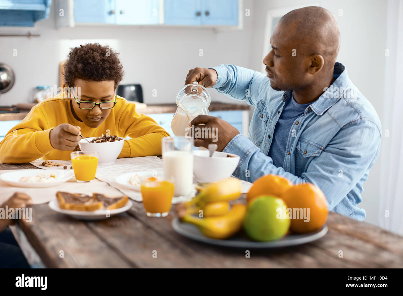 Agréable jeune homme verser le lait, tout en fils de manger les céréales Banque D'Images