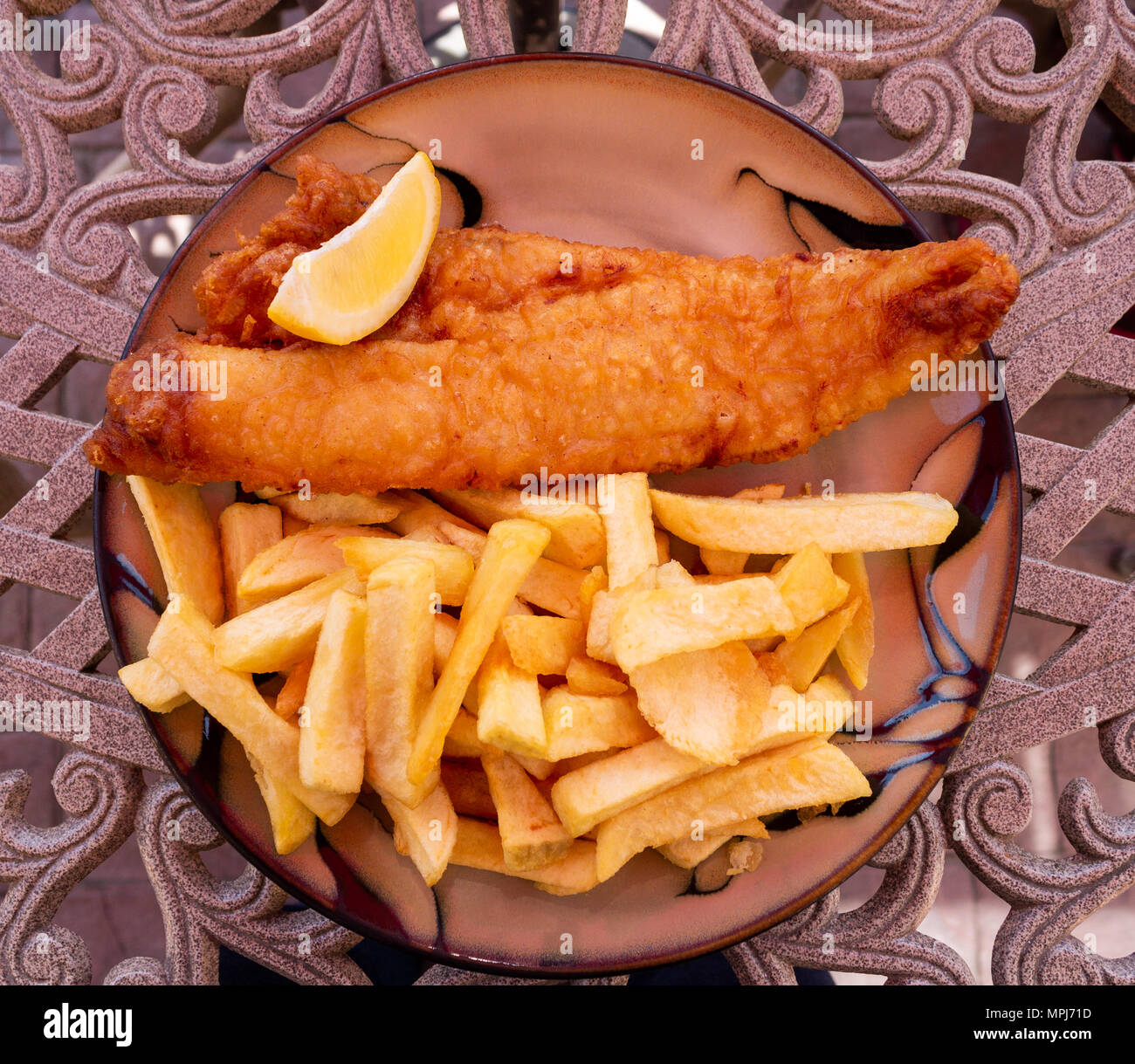 Repas de poisson et frites avec un quartier de citron ou de citron sur filtre en coin d'une table. Banque D'Images