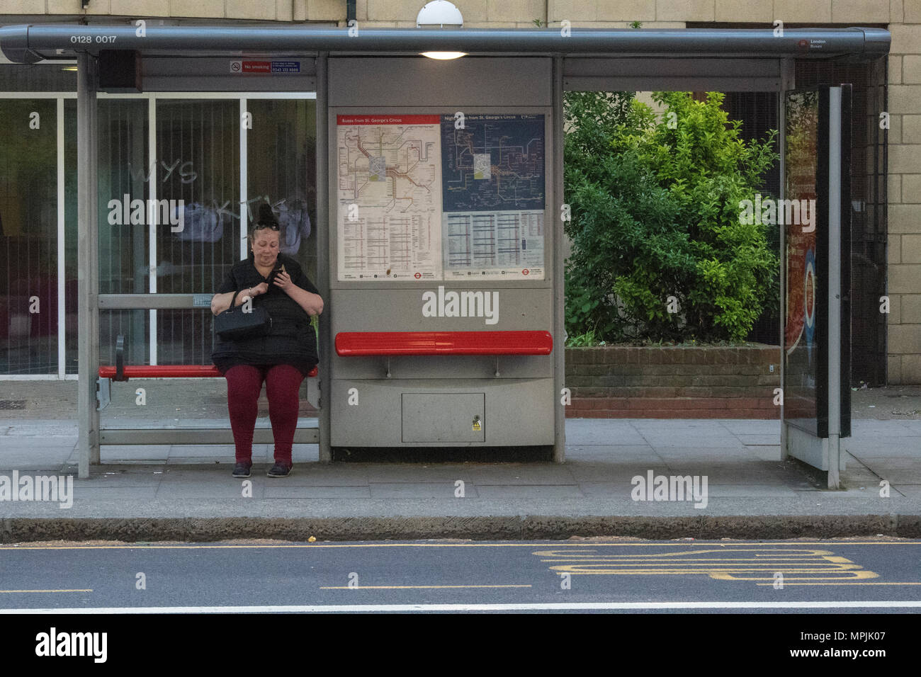 Une grande dame en attente d'un bus à un arrêt de bus dans le centre de Londres à l'aide de téléphone mobile ou portable smartphone pour envoyer et recevoir un SMS ou email. bus. Banque D'Images