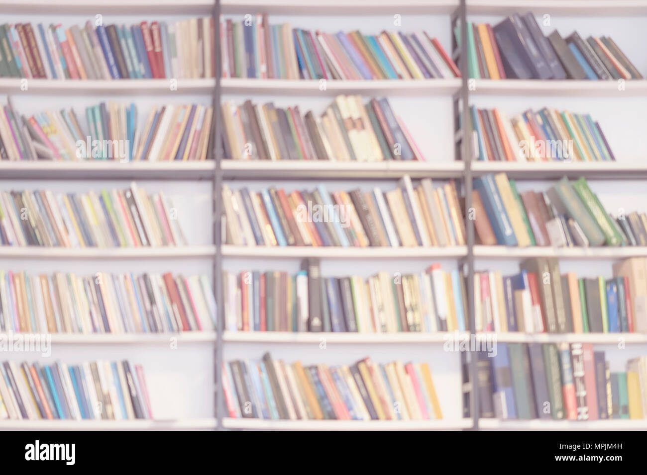 De nombreuses rangées de livres colorés en blanc, lumière floue fond abstrait. Étagères de trouble bibliothèque avec livres, l'étude, de l'éducation. Filtre la lumière, l'effet Soft focus Banque D'Images