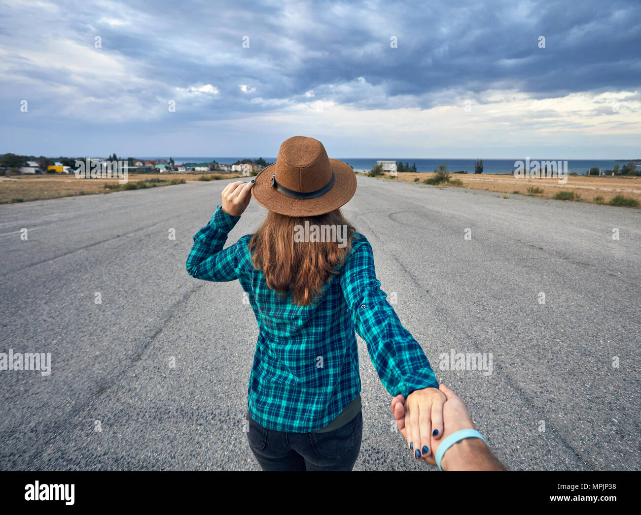 Heureux couple in checked shirt holding par les mains et marcher sur la large route asphaltée avec lac et fond de ciel nuageux Banque D'Images