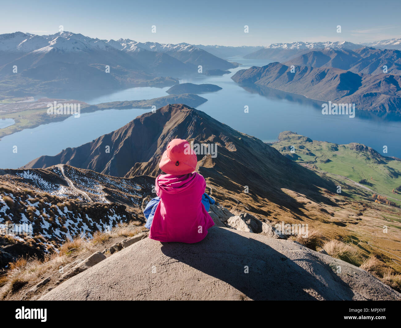 Jeune femme assise au bord de la falaise à la vue panoramique sur les montagnes et les lacs de Roys Peak, Nouvelle-Zélande Banque D'Images