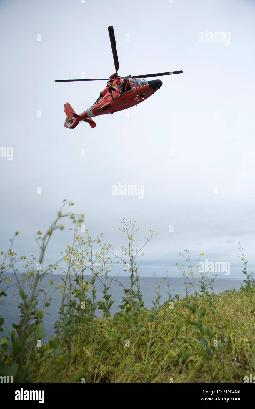 Un nageur de sauvetage de la Garde côtière canadienne affectée à la base d'opération avancée Point Mugu est abaissé d'un MH-65 hélicoptère Dauphin sur une falaise au cours de la formation en sauvetage au point Vicente Lighthouse 21 mars 2017. La formation permet de garder d'équipage compétent dans le cas d'un monde réel côté falaise de sauvetage. (U.S. Photo de la Garde côtière canadienne par le maître de 3e classe Andrea Anderson/libérés) Banque D'Images