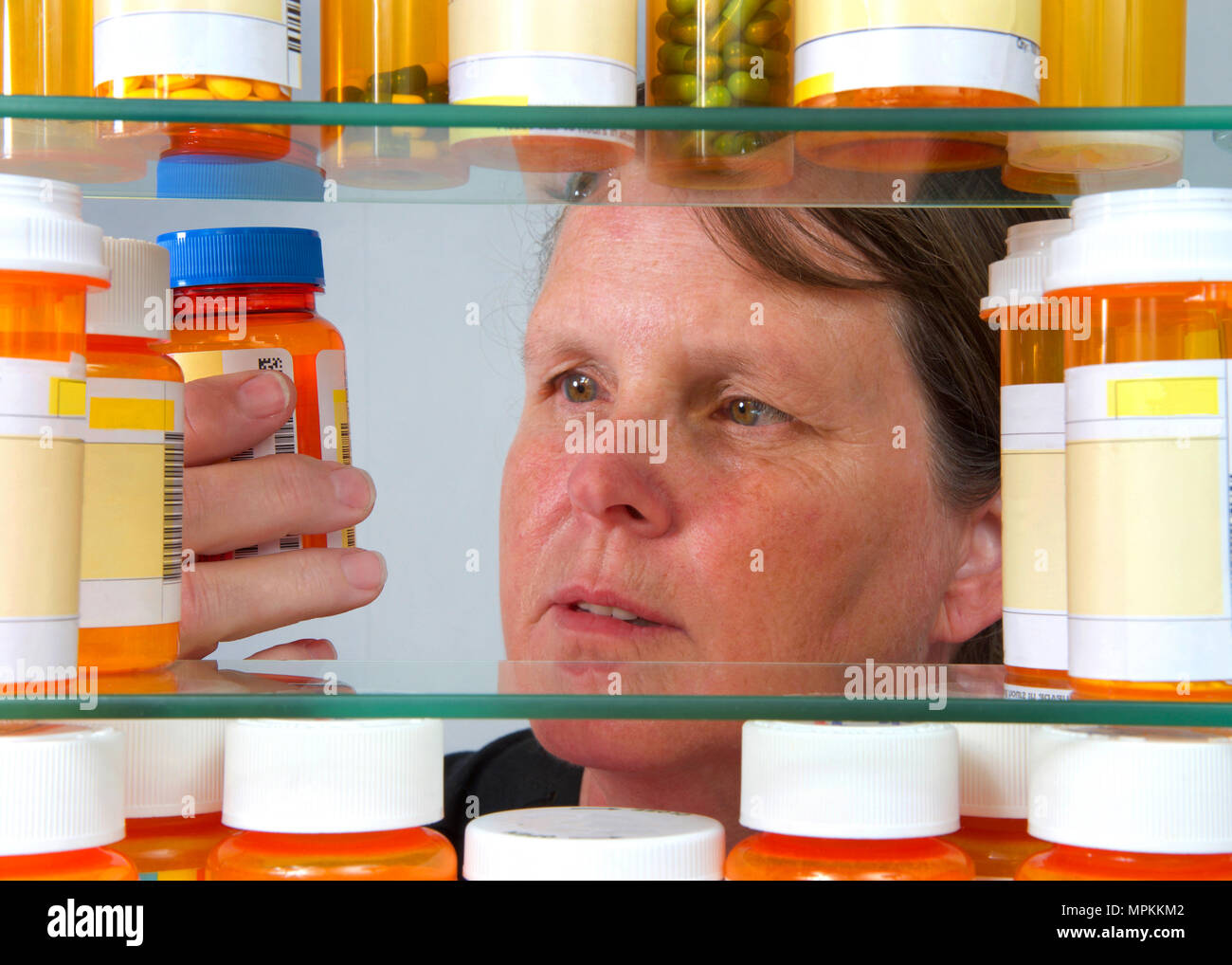 Middle aged woman reading de l'étiquette des médicaments sur prescription bottle in medicine cabinet, vue depuis l'intérieur du cabinet med. Concept de bien-être, Banque D'Images
