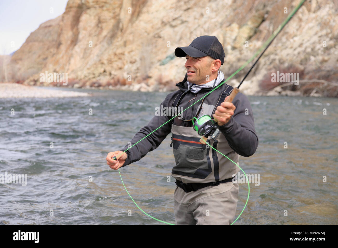 pêcheur adulte de sexe masculin qui se coud à gué et jette une tige de mouche une rivière Banque D'Images