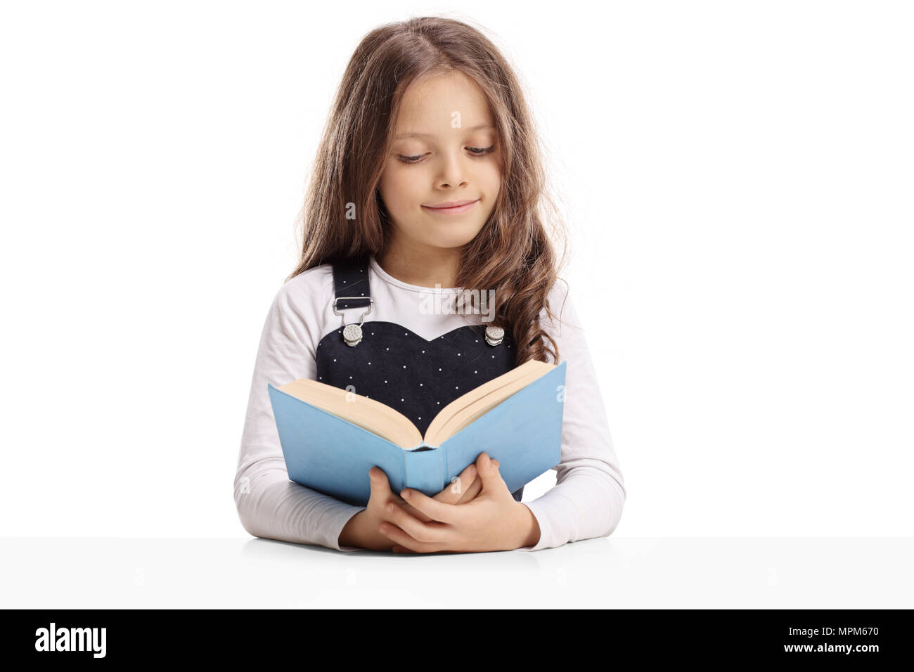 Petite fille assis à une table pour lire un livre isolé sur fond blanc Banque D'Images