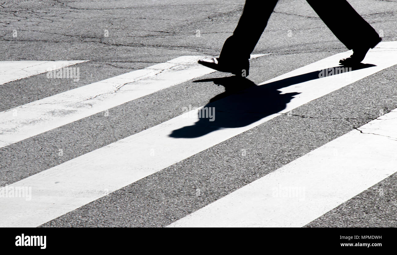 Rue de la ville floues zebra crossing avec un piéton en marche les jambes de silhouette dans l'ombre haut contraste noir et blanc Banque D'Images