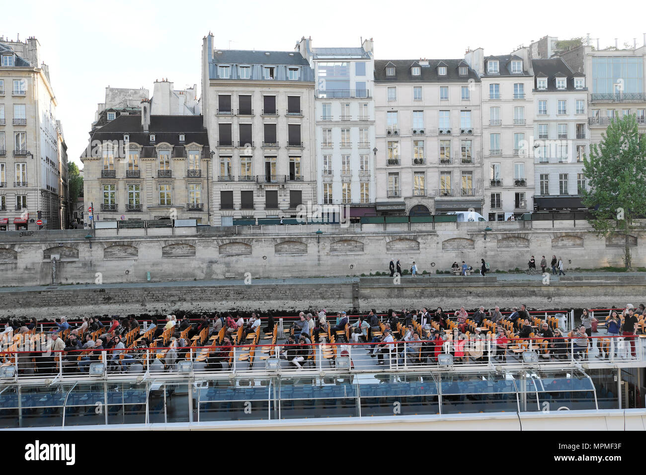 Bateau de tourisme touristes avec des gens assis sur le pont passant d'une rangée de bâtiments en terrasses et le quai, le long de la Seine à Paris France UE KATHY DEWITT Banque D'Images