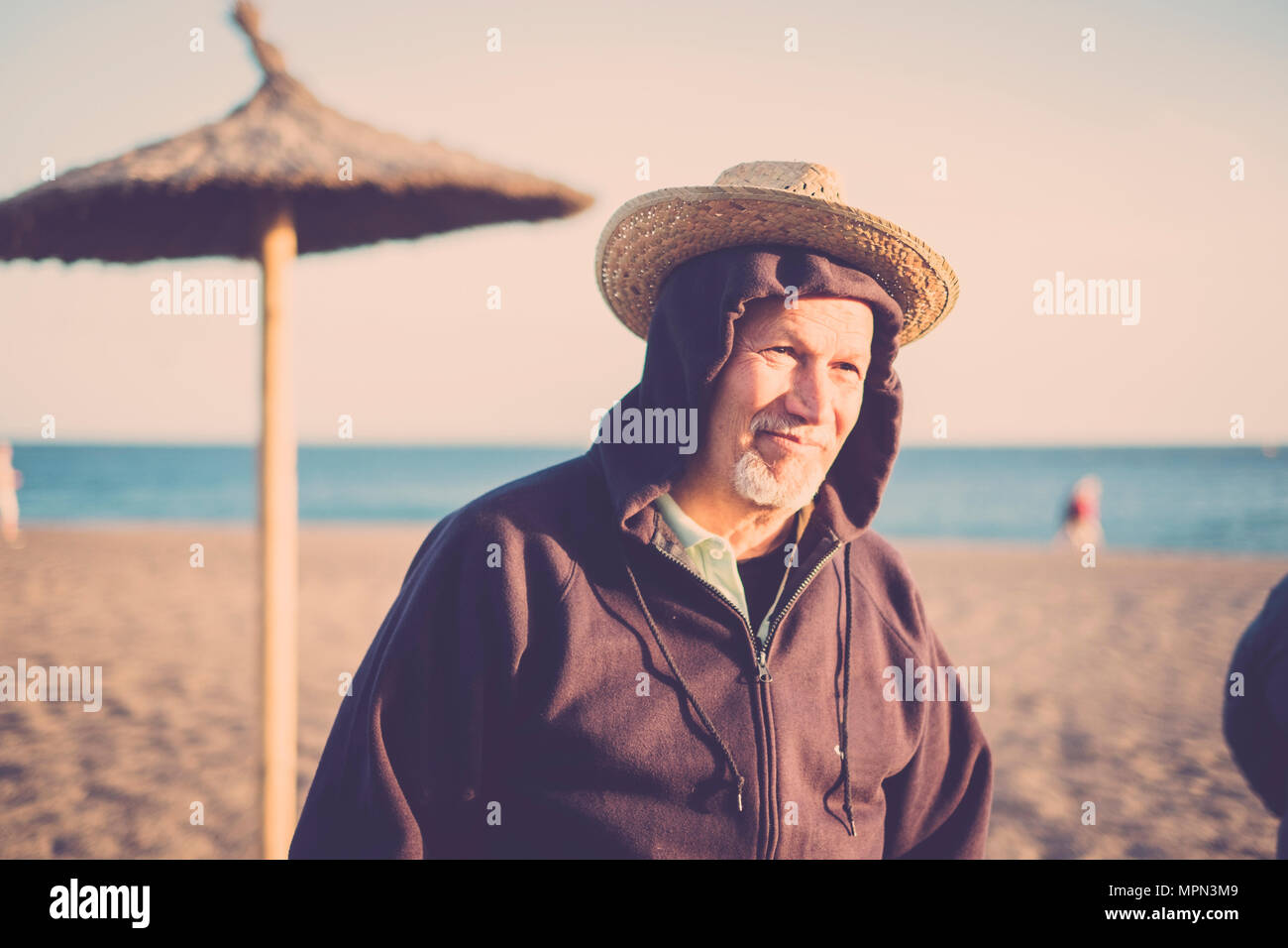 Belle funny senior homme à double casquette à la plage en hiver. vintge tons. sourire et lumière sur le visage ensoleillé Banque D'Images