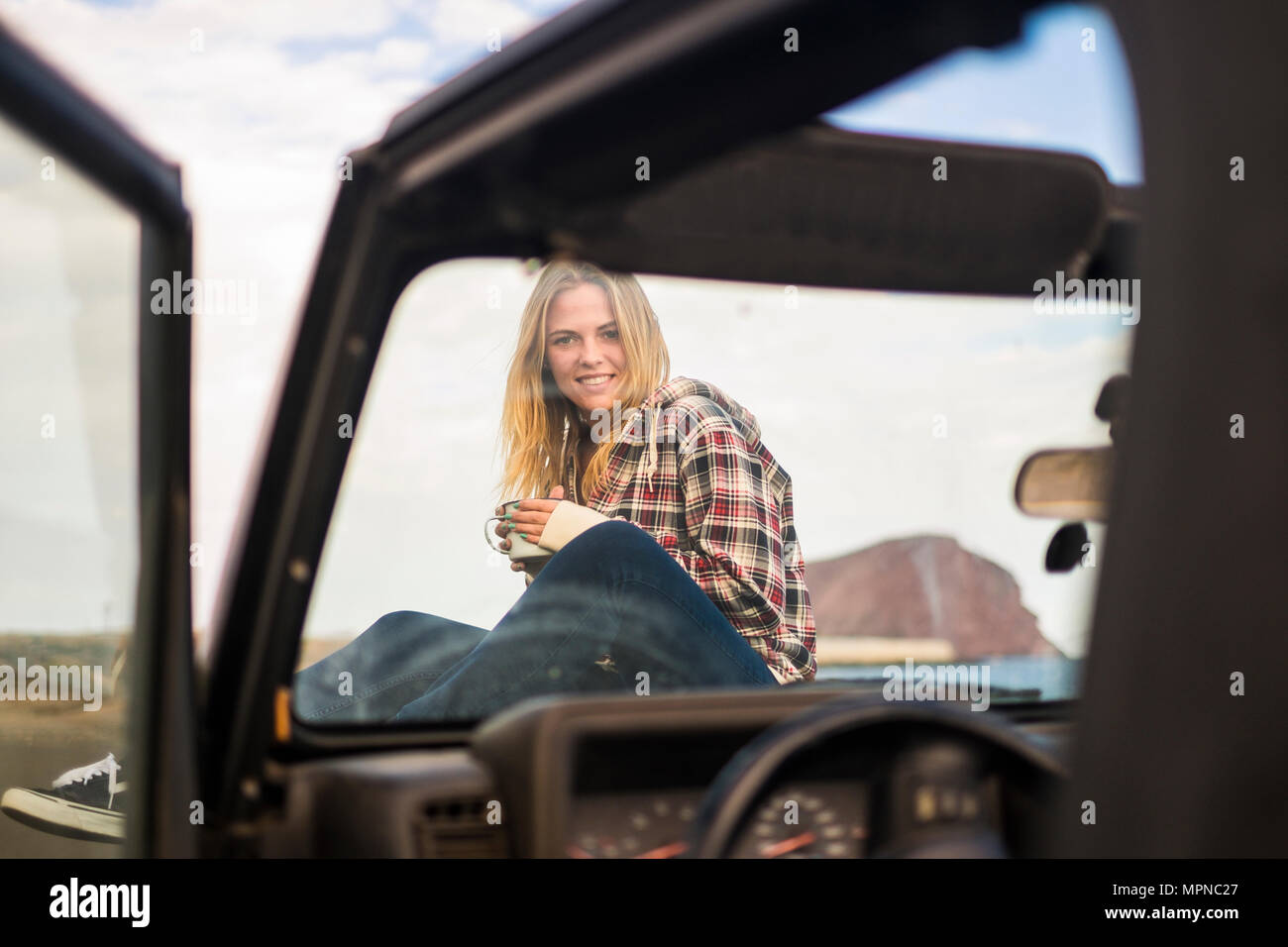 La liberté et vacances pour belle blonde portrait jeune femme assis sur le nez d'un off road voiture noire. Rétro-éclairage et de la lumière du soleil à wa Banque D'Images