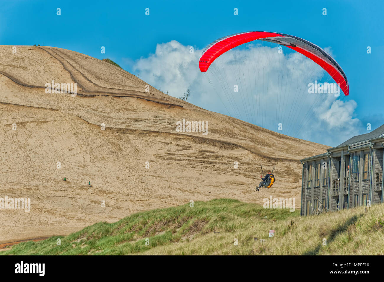 Un deltaplane les pilotes son cerf-volant passé une rangée d'appartements sur une colline herbeuse avec de grandes dunes de sable à l'arrière-plan de Cape Kiwanda dans Pacific City sur l'Ore Banque D'Images