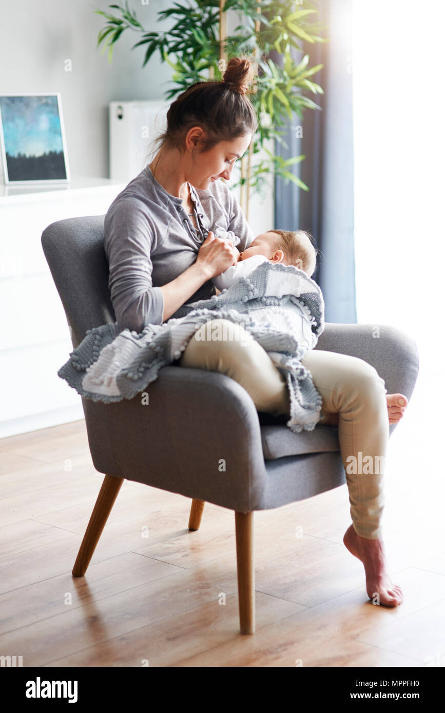 Mère assis sur un fauteuil à la maison d'allaiter son bébé Banque D'Images